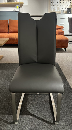 Schwingstuhl „Mirafor“ in Grau, gebürsteter Edelstahl auf Teppichboden, orangefarbenes Sofa im Hintergrund.