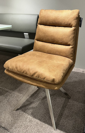 Stuhl „Mondo Natur Folara“ auf einem Teppich neben einer grauen Bank und einem Tisch, mit Edelstahlbeinen und brauner Mikrofaser-Polsterung.