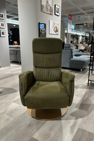 Ein grüner Relaxsessel Planoform Maggio mit Polyätherschaum steht vor Sofas und einem Holzdrehteller aus Eiche Bianco.