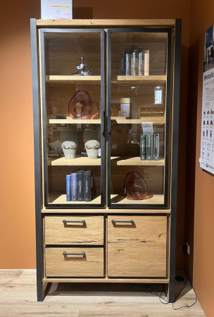 Die Vitrine „Metalo“ mit Glastüren und LEDs präsentiert Bücher und Dekoartikel vor einer orangefarbenen Wand.