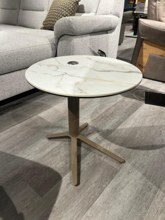 Beistelltisch Hagen mit Glasplatte in Keramikoptik und Gestell aus Metall in Bronze, neben einem grauen Sofa auf einem Holzboden.