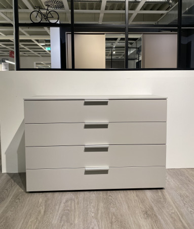 Die Kommode „Monda Design Ajana Scale“ mit vier Schubladen steht auf einem Holzboden in einem minimalistisch eingerichteten Raum.