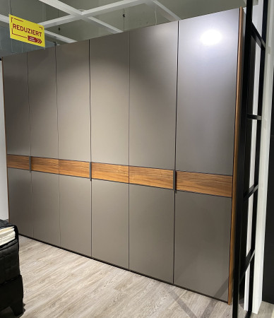 Drehtürenschrank „Mondo Easymax 100“ in Grau mit Akzenten in Kernnussbaum unter einem „Reduziert“-Schild auf einem Holzboden.