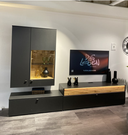Wohnwand „Lumea“ in Anthrazit matt/Eiche gehackt mit Beleuchtung, Glaswaren, Deko, Fernseher „Das Leben“ und Standuhr.
