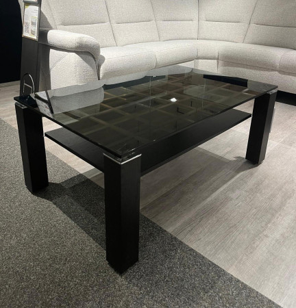 Couchtisch CUBICO aus schwarzem Rauchglas mit vier dicken Beinen, auf einem grauen Teppich neben einem hellgrauen Ecksofa.