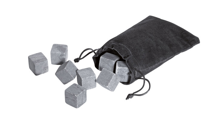 Die Kühlsteine Cool Rocks aus grauem Granit sind Whiskey-Steine, die aus einem schwarzen Kordelzugbeutel auf eine weiße Fläche fallen.