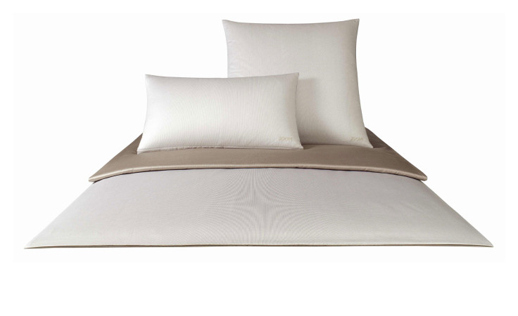 Ein ordentlich gemachtes Bett mit Joop Mako-Satin Kissenbezug 40x80 cm, zwei cremefarbenen Kissen und einer beige-cremefarbenen Bettdecke auf Weiß.