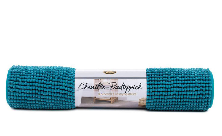 Ein aufgerollter Gözze Badteppich Chenille 60 x 100 cm, mit einem deutschen Etikett, auf weißem Grund.