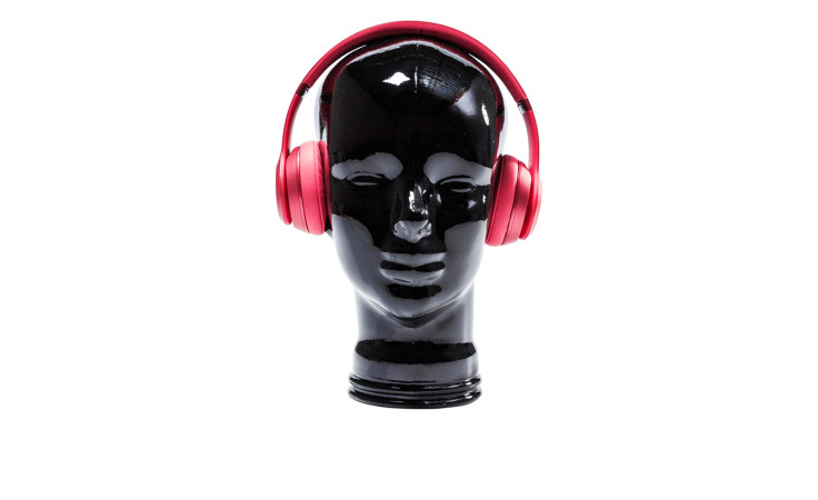 Kare Kopfhörerständer in glänzendem Schwarz mit roten Over-Ear-Kopfhörern auf weißem Hintergrund.