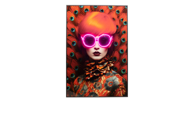 Frau mit orangefarbenem Haar, geblümtem Kleid und neonpinker Sonnenbrille vor Kare's LED-Rahmenbild Fancy Red Lady 80x120 cm.