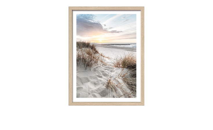Das Pro-Art Rahmenbild Nordische Strandatmosphäre 33 x 43 cm zeigt einen Sandstrand, hohes Gras und einen bunten Himmel bei Sonnenuntergang.