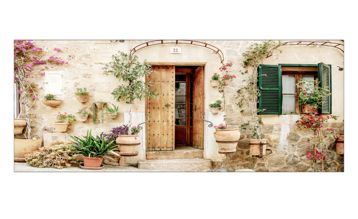 Pro-Art Glasbild Mediterranean House 30x80 cm zeigt eine Steinfassade, grüne Fensterläden, Blumen und Glastöpfe an der Wand.