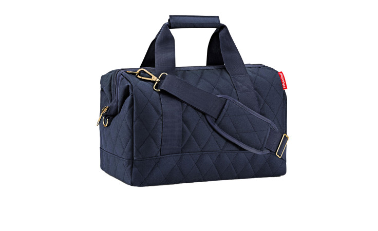 Die Reisenthel Reisetasche Allrounder M ist ein gesteppter marineblauer Seesack mit Griffen und einem abnehmbaren Riemen auf weißem Grund.