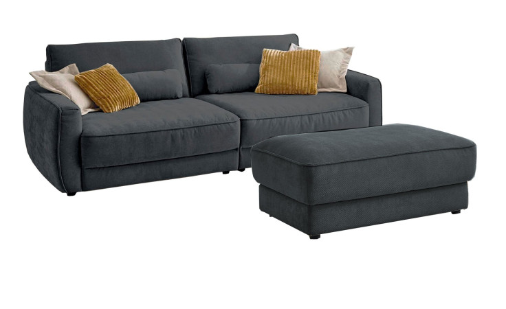 Komfort-Big Sofa planoform Cochem in der Farbe Grau mit mehreren Kissen, zwei davon sind braun, und der passende Hocker dazu