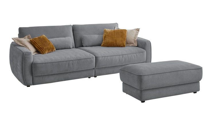 Komfort-Big Sofa planoform Cochem in der Farbe Hellgrau mit mehreren Kissen, zwei davon sind braun, und der passende Hocker dazu