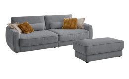 Komfort-Big Sofa planoform Cochem in der Farbe Hellgrau mit mehreren Kissen, zwei davon sind braun, und der passende Hocker dazu