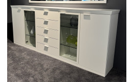 Sideboard „Vilano Sonate“, 240 × 96 × 40 cm, mattweiß, 5 Schubladen, Glasvitrinen, auf grauem Teppich.