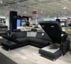 Ecksofa Planoform Nizza mit Federkern, offenes Staufach, abgebildet unter heller Ausstellungsbeleuchtung.