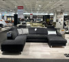 Dunkelgraues Ecksofa Planoform Nizza mit Federkern, Stoff Vincent, abgebildet mit Kissen in einer Ausstellungsumgebung.