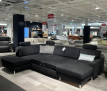 Großes anthrazitfarbenes Ecksofa Planoform Nizza mit Federkernpolsterung und Kissen, ausgestellt in einem modernen Showroom.