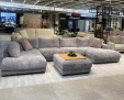 Wohnlandschaft „Hagerstown“: Großes graues Sofa mit Rückenkissen, Ottomane und rosa Kissen im Ausstellungsraum.