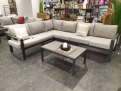 Graues L-förmiges Sofa mit „Sunproof“-Kissen in Grau, neben einer Gartentisch-Gruppe „Mondo Nilson/Belinda“ im Ausstellungsraum.