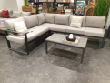 Graues Ecksofa mit „Sunproof Kissen grau“ und der Gartentisch-Gruppe „Mondo Nilson/Belinda“ auf Steinboden.