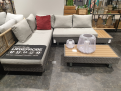 Lounge-Set „Rügen 2“ – graues Sofa, rotes Kissen, Couchtisch aus Polywood und weiße Deko in einem modernen Showroom.
