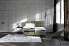 Modernes Schlafzimmer mit einem Tempur-Boxspringbett „Discovery Classic“ in Samtoptik, einem Samtstuhl, einem Teppich und großen Fenstern.
