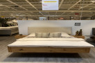 Das Bett mit Nachttischen (Freiburg 11) mit beigem Kopfteil wird in einem modernen Möbelausstellungsraum präsentiert.