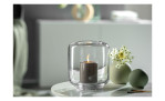 Eine brennende Kerze in einem Glashalter steht neben der Leonardo Vase Bolla 9 cm mit weißen Blumen auf dem Tisch.