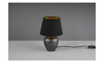 Die Reality Tischleuchte Abby 18 cm mit schwarzem Schirm steht auf einer grauen Fläche vor einem grauen Hintergrund.