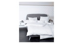 Mako-Satin Kissenbezug Colors in er Größe 40 x 40 cm und in einer weißen Farbausführung, auf einem Bett bezogen mit der passenden Bettwäsche und anderen Kissen.