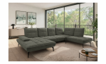 Modernes Wohnzimmer mit der Vito Komfort-Wohnlandschaft „vito Ticona Plus“, einem runden Teppich, einem Couchtisch und großen Fenstern.