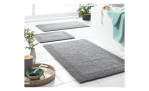 Drei Casa Nova Badteppiche Cleveland 60 x 90 cm liegen in Grau auf weißen Fliesen mit Pflanzen und Accessoires.