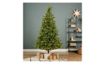 Grüner Tannenbaum Allison II 240 cm, Ø152 cm, mit Lichtern und Geschenken neben Regal mit Stern.