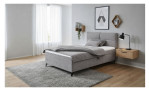 Graues, gepolstertes Boxspringbett Carmen mit einer grauen Bettdecke, platziert auf einem grauen Teppich in einem modernen Schlafzimmer.