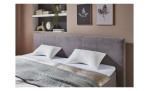 Ein ordentlich gemachtes Bett mit einem „Schlafkissen Easydream“, einem grauen Kopfteil, Wandbildern und Regalen mit Büchern darüber.