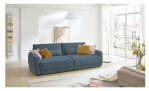 Komfort-Big Sofa planoform Cochem in der Farbe Blau mit mehreren Kissen, zwei davon sind braun, und der passende Hocker dazu in Weiß ist teilweise zu sehen,im Wohnzimmer