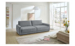Komfort-Big Sofa planoform Cochem in der Farbe Hellgrau und der passende Hocker dazu in Weiß ist teilweise zu sehen, im Wohnzimmer