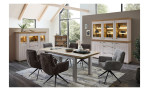 Modernes Esszimmer mit dem Komfort-Buffet Cornwall, sechs grauen Stühlen, einem Holztisch, beleuchteten Vitrinen, großen Fenstern und einer neutralen Einrichtung.