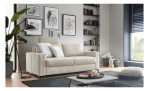 Das Hukla Komfort-Schlafsofa „Pickering“ mit Kissen in einem modernen Zimmer, Wanddekoration, Pflanzen, Regalen und einem Fenster mit schwarzen Jalousien.