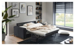 Ein modernes Wohnzimmer mit dem Hukla Komfort-Schlafsofa „Pickering“, kunstvoll gestalteten Wänden, Bücherregalen und großen Fenstern.