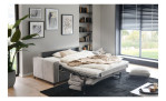 Das ausgeklappte Basis-Schlafsofa „Pickering“ von Hukla mit Bettwäsche in einem modernen Wohnzimmer mit großen Fenstern und Wandbildern.