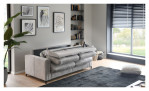 Ein graues „Basis“-Schlafsofa „Pickering“ von Hukla steht halb ausgeklappt in einem modernen Wohnzimmer mit Kunstwerken und großen Fenstern.
