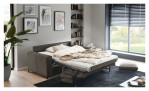 Basis-Schlafsofa „Pickering“ von Hukla mit beiger Bettwäsche und Metallgestell in einem modernen Wohnzimmer neben großen Fenstern.