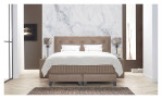 Komfort-Boxspringbett Premium Magnifique in einem Bezugsstoff in Beige. Auf einem dekorierten Hintergrund