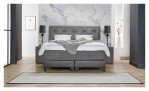 Basis-Boxspringbett Premium Magnifique mit einem Bezugsstoff in Grau. Auf einem dekorierten Hintergrund