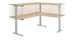 Elektro-Winkelschreibtisch mit holzfarbener Tischplatte und silbernem Gestell. Tischplatte in allen Höhen übereinander dargestellt.
