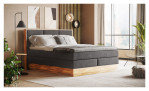 Boxspringbett MONDO NATUR Incana in einem Stoffbezug in Dark Grey und einem Sichtholzrahmen in Eiche. Auf einem dekorierten Hintergrund